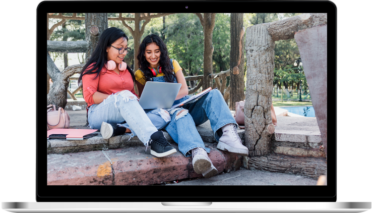 Dos chicas sonrientes mirando la computadora al aire libre